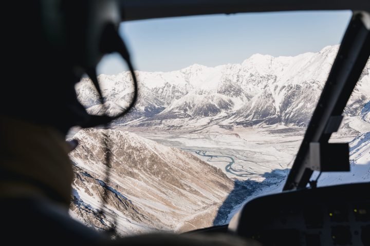 Helicopter Pilot looking out Window to River and Snowy Mountains
