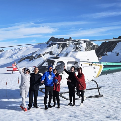 a group of people stand in front of ski plane and helicopter on tasman glacier in the southern alps