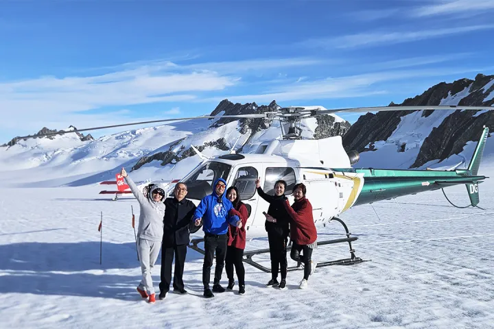 a group of people stand in front of ski plane and helicopter on tasman glacier in the southern alps