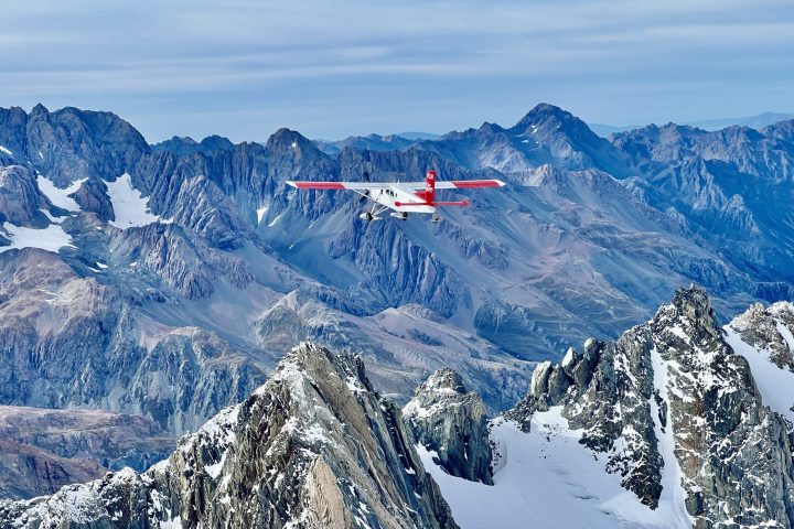White ski plane flies across snowy mountain range in Mountain Cook