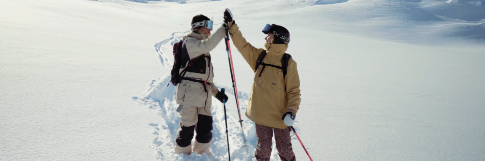 Two skiers in snow gear high-five on a snowy slope.