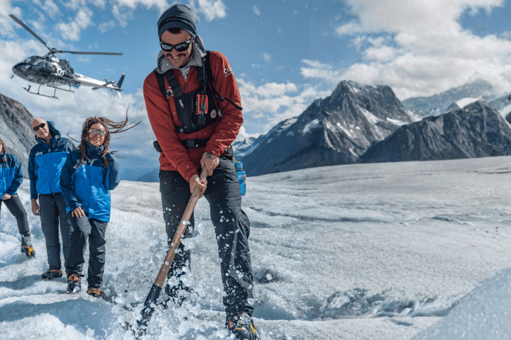 People on a snowy mountain with an axe, helicopter flying in the background.