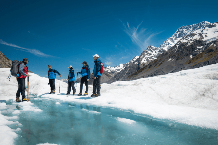 Group of hikers on a glacier near a mountain under a clear blue sky.
