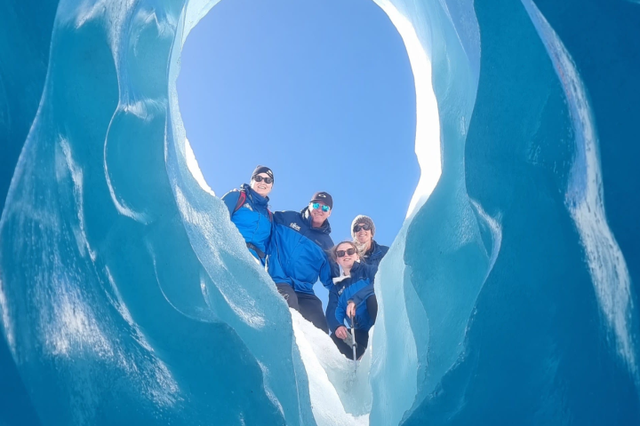 Four people in blue jackets inside an icy cave looking towards the camera.