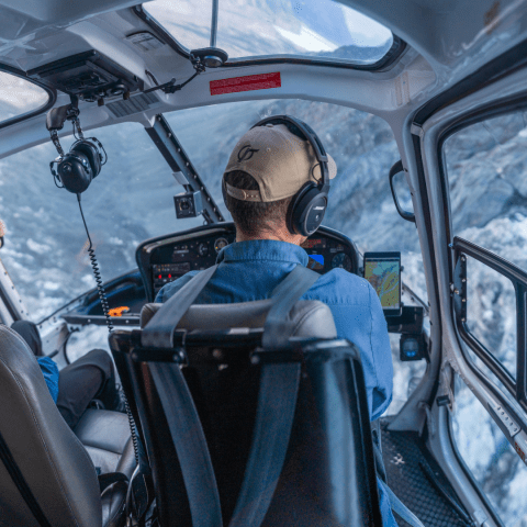 Interior of a helicopter with two pilots flying over a snowy mountain landscape.