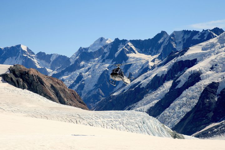 a view of a snow covered mountain with a helicopter in the air