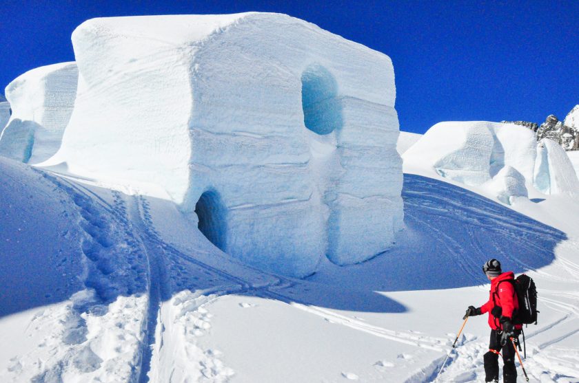 a man riding skis down a snow covered tasman glacier beside ice formation