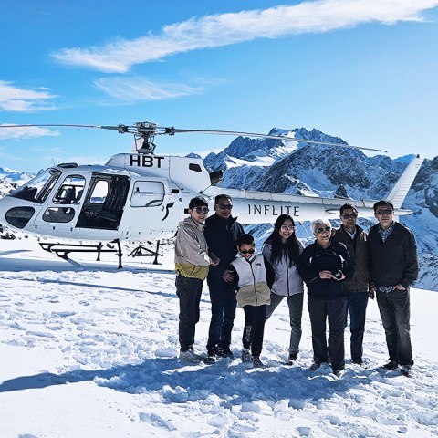 A group of tourists stand in front of helicopter on a Tasman Glacier tour with new zealand mountains in the background
