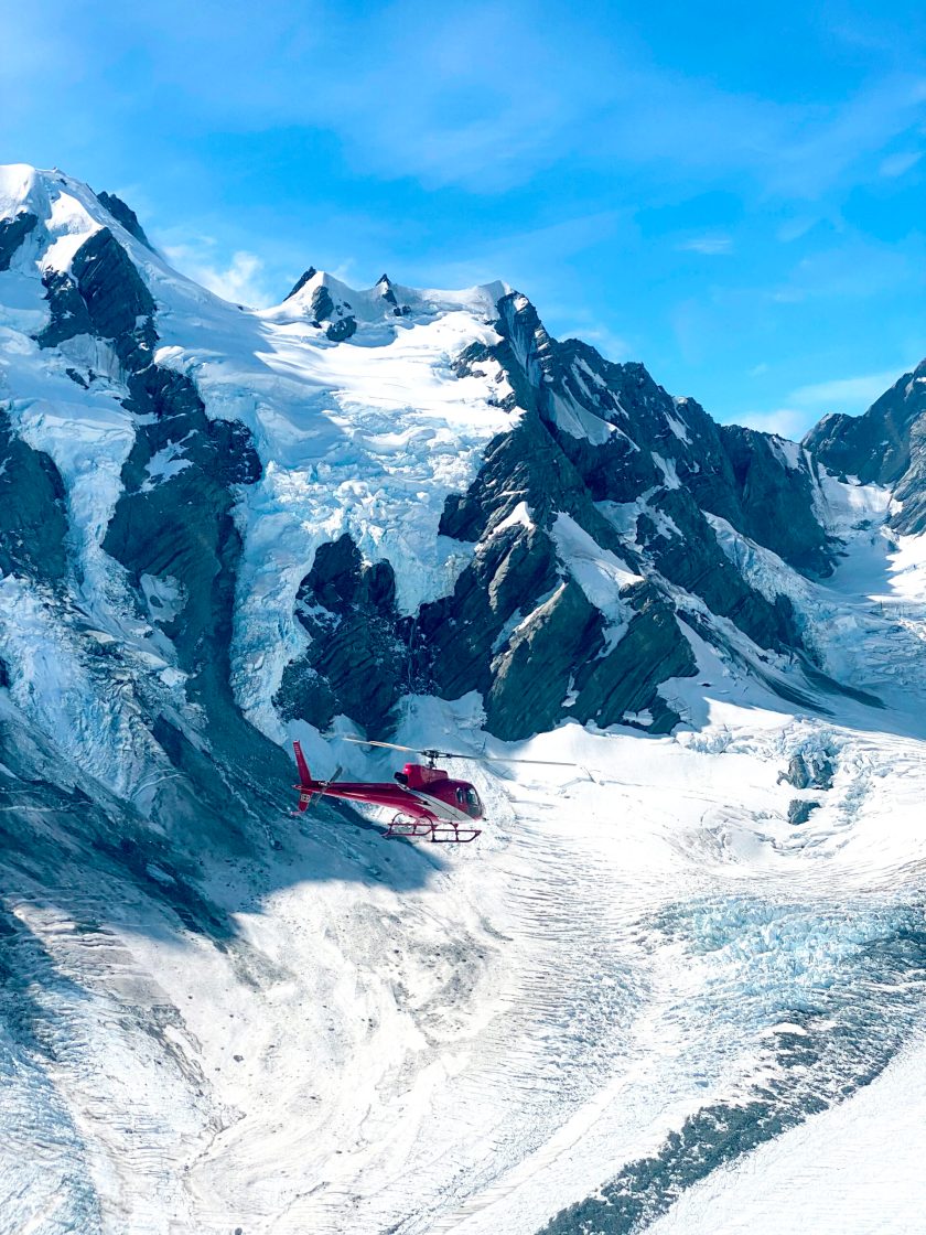 Red Inflite Helicopter flys tourists through the mountains and over Tasman glacier from West Coast of New Zealand