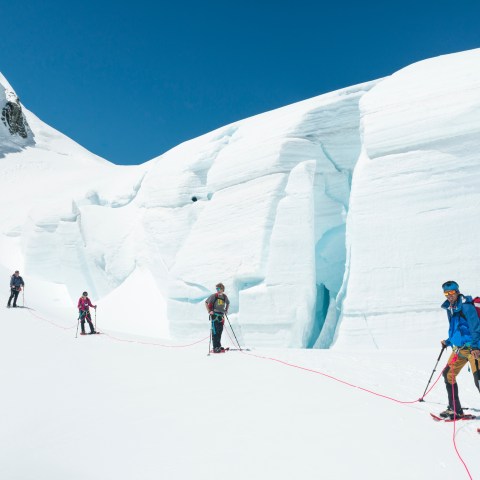 Four climbers roped together on a snowy mountain with a large ice formation.