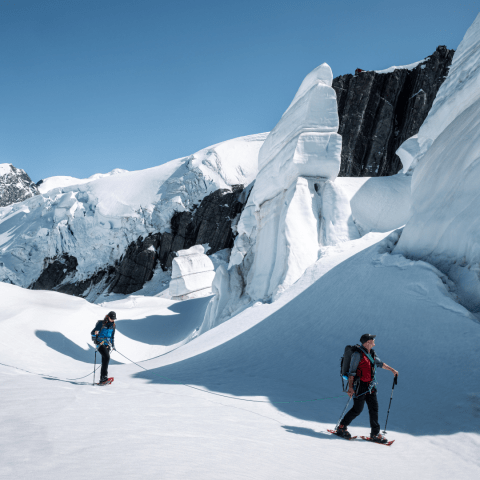 People hiking on a snow-covered mountain with large ice formations and a clear blue sky.