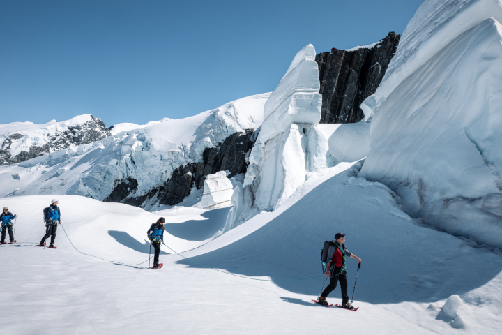 People hiking on a snow-covered mountain with large ice formations and a clear blue sky.