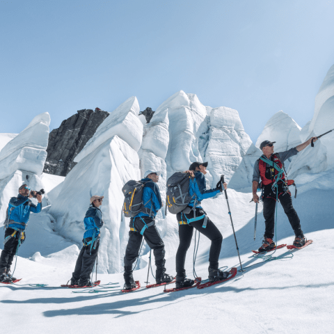 Five people snowshoeing on a snowy mountain with ice formations in the background.