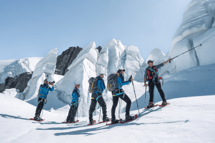 Five people snowshoeing on a snowy mountain with ice formations in the background.