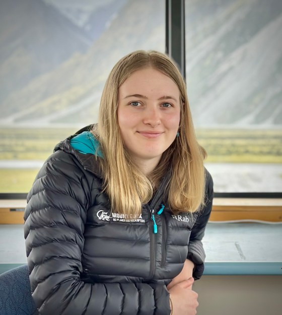 Person in a black jacket sitting indoors with a mountain view through the window.