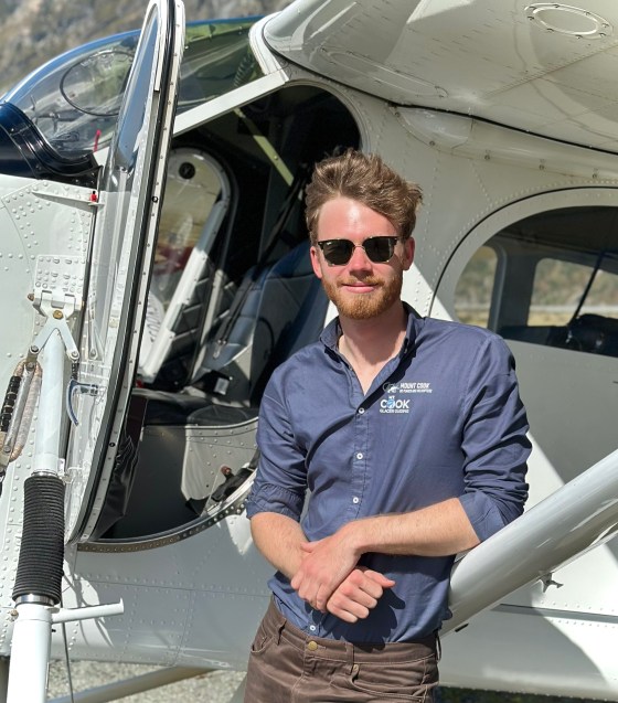 Person in sunglasses leaning on a small aircraft with an open door.