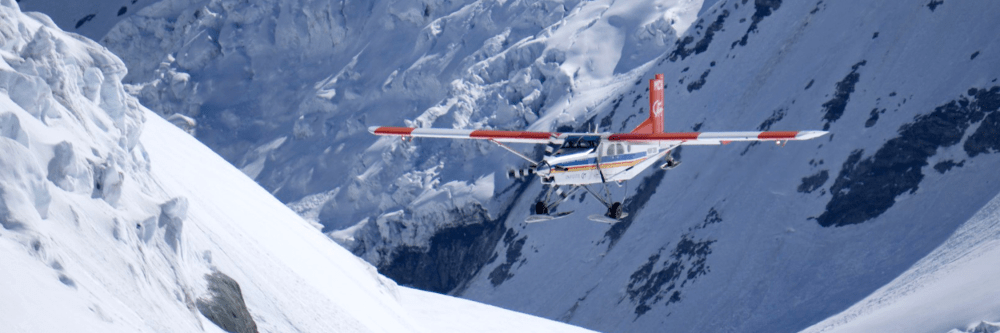 Small plane flying over snowy mountain terrain.