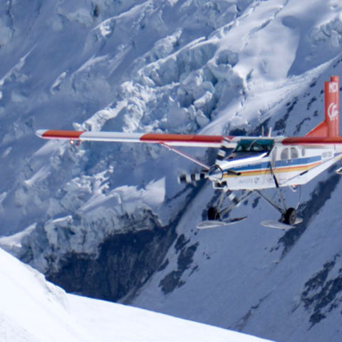 Small plane flying over snowy mountain terrain.