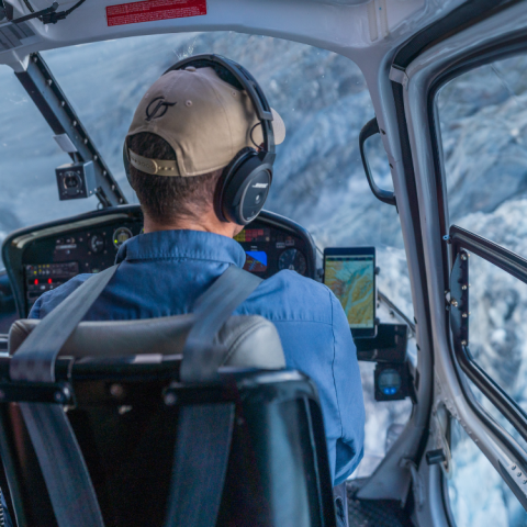Two pilots in a helicopter cockpit flying over snowy mountains.