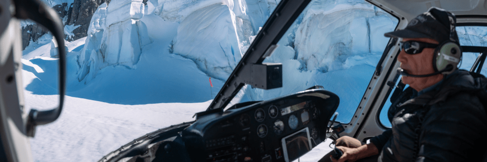 Helicopter pilot flying near snowy mountains with glaciers.