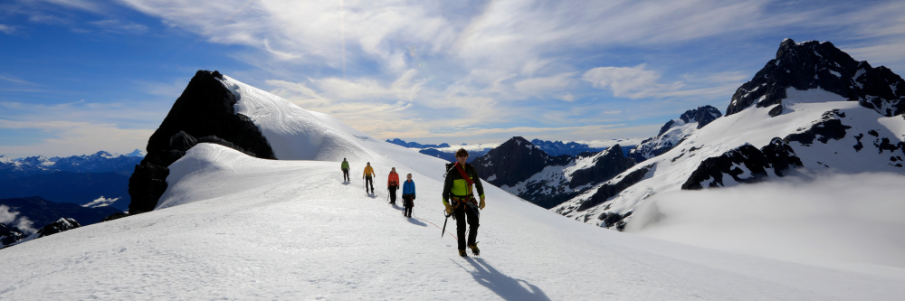 People hiking on snowy mountain ridge under clear blue sky.