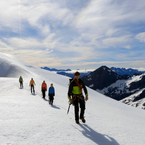 People hiking on snowy mountain ridge under clear blue sky.