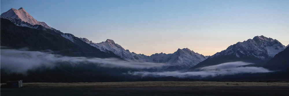 Snow-capped mountains at dusk with clouds in valleys.