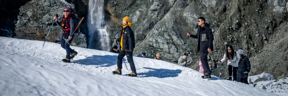 Group of people hiking on a snowy mountain slope near a waterfall.